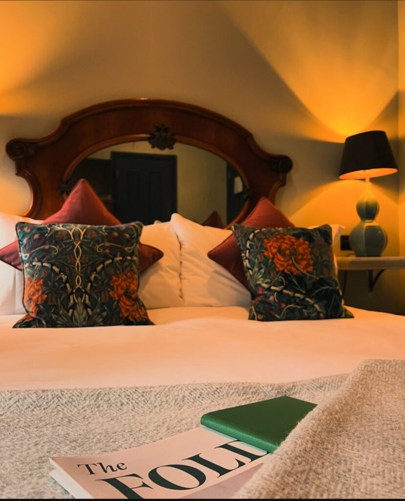 A warmly lit bedroom at The Wheatsheaf, with patterned cushions and a carved wooden headboard