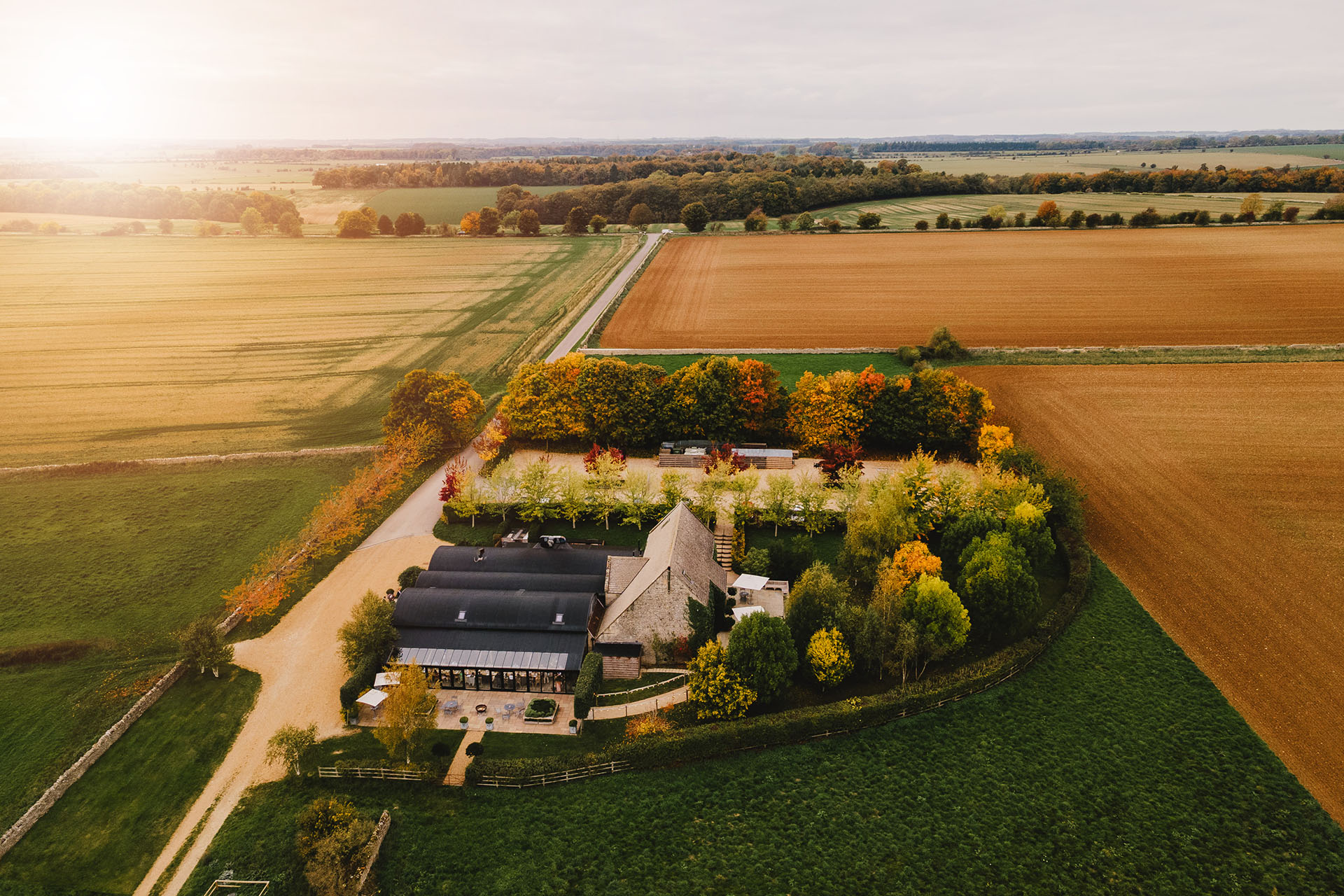 Aerial view of Stone Barn surrounded by trees and Cotswold countryside in golden evening light